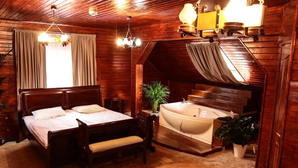 A wooden room with a bed, a bench, a small table, a plant, and a bathtub. - Hotel Apollonia (Brasov)