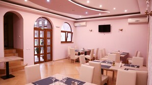A dining area with multiple tables and chairs, an exit door, and a television mounted on the wall. - Hotel Apollonia (Brasov)