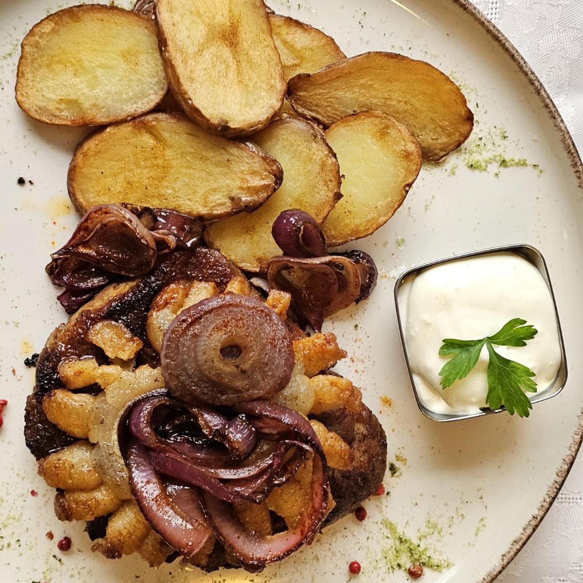 Um prato com batatas assadas, cebolas e uma pequena tigela de molho.