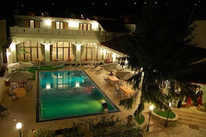 A hotel with a swimming pool, outdoor seating, and a covered patio area.