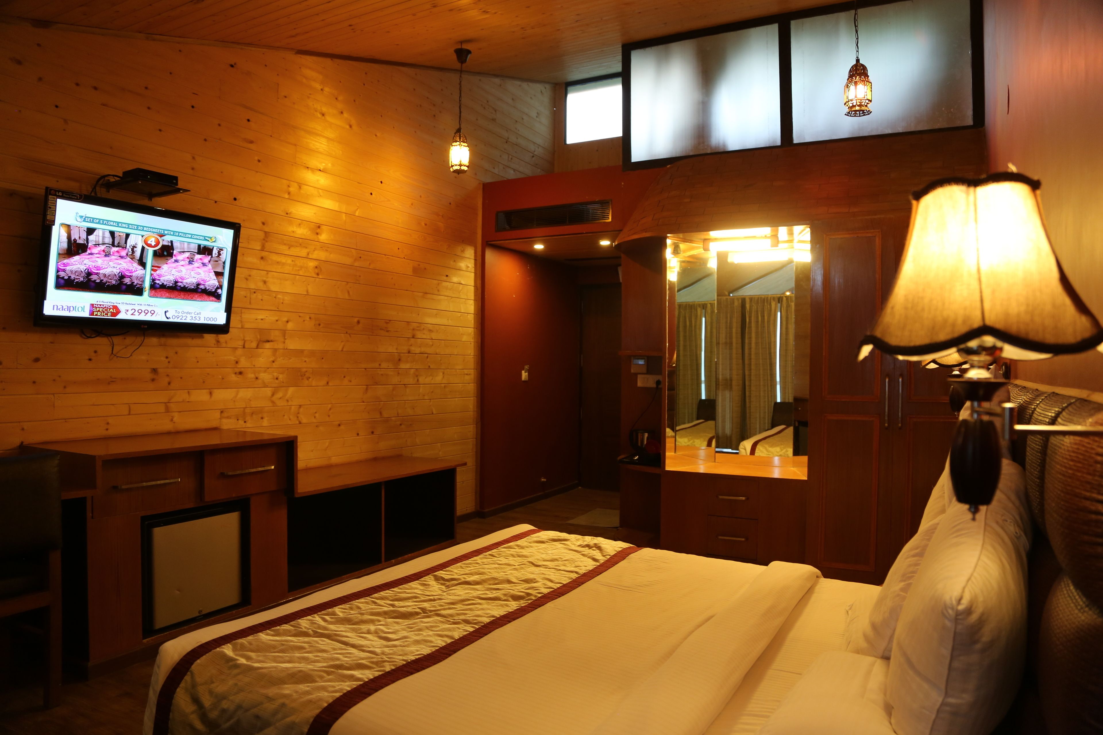 A hotel room with a bed, a television mounted on the wall, a desk, and a mirror.
