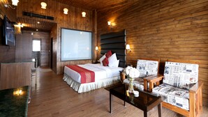 A wooden cabin-style room with a bed, a desk, and a seating area with newspaper-covered cushions. - Winnies (Kasauli)