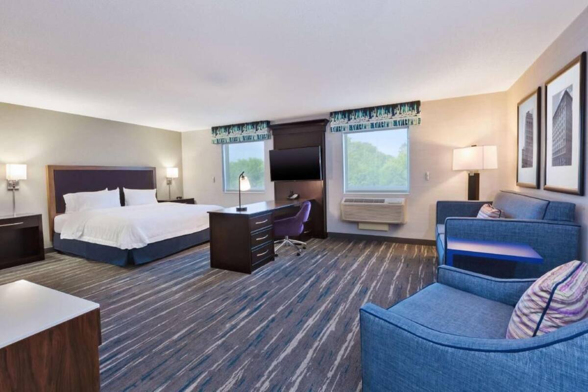 A hotel room with a bed, desk, chair, and a sofa.
