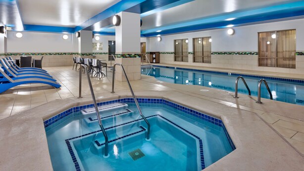 A hotel pool area with a large rectangular pool, lounge chairs, and a seating area with tables and chairs.