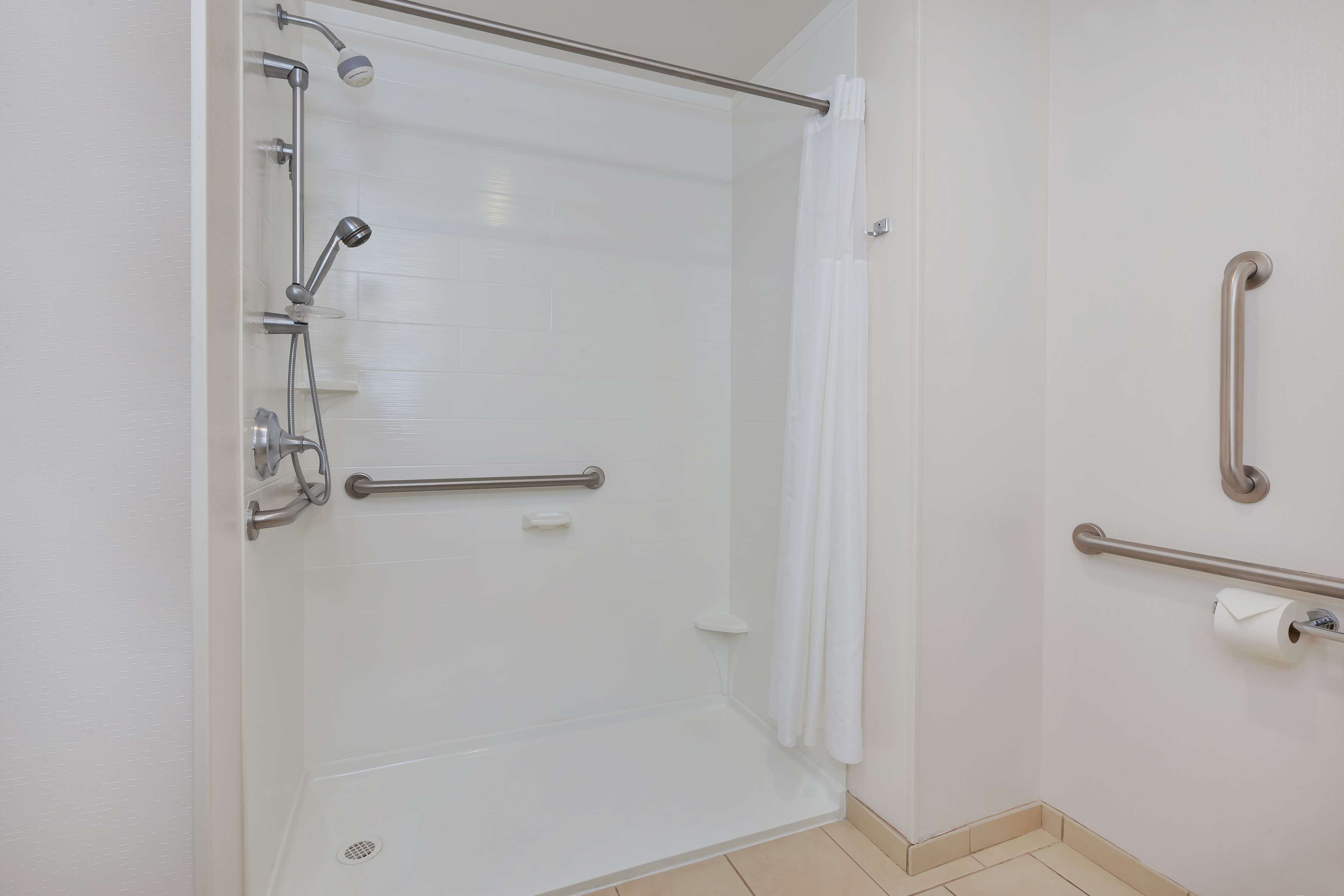 A bathroom with a shower, grab bars, and a toilet paper holder.