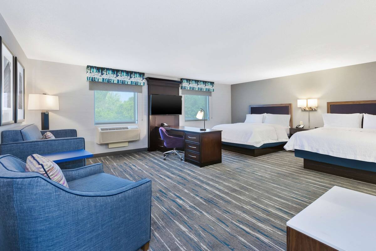 A hotel room with a bed, a desk, a chair, a sofa, and a large window.