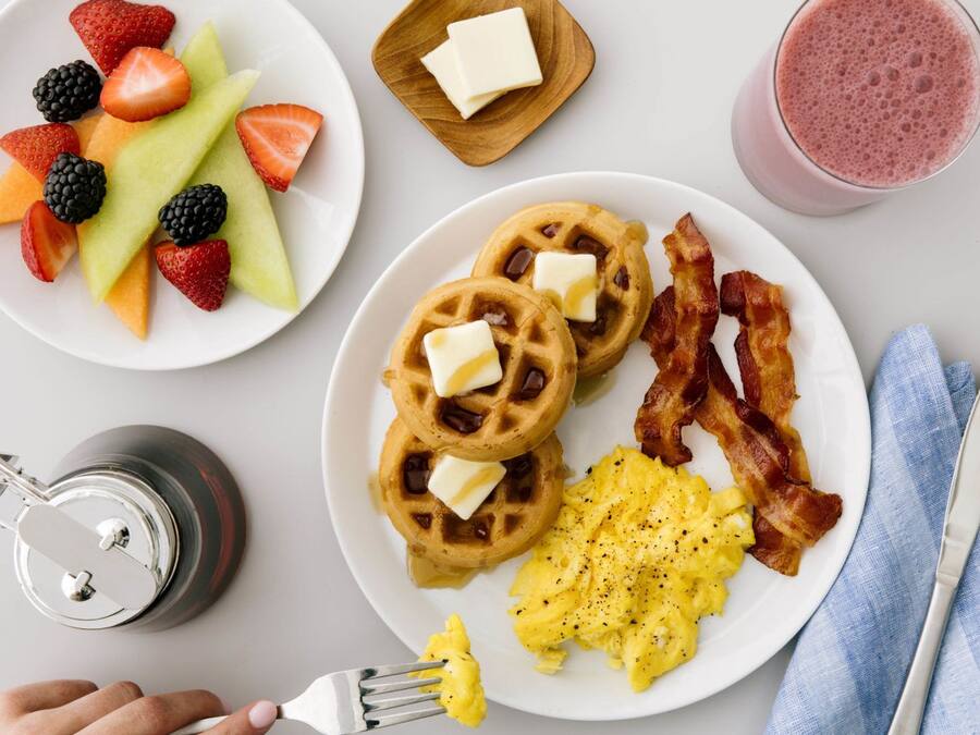 A breakfast plate with waffles, scrambled eggs, bacon, and fruit.