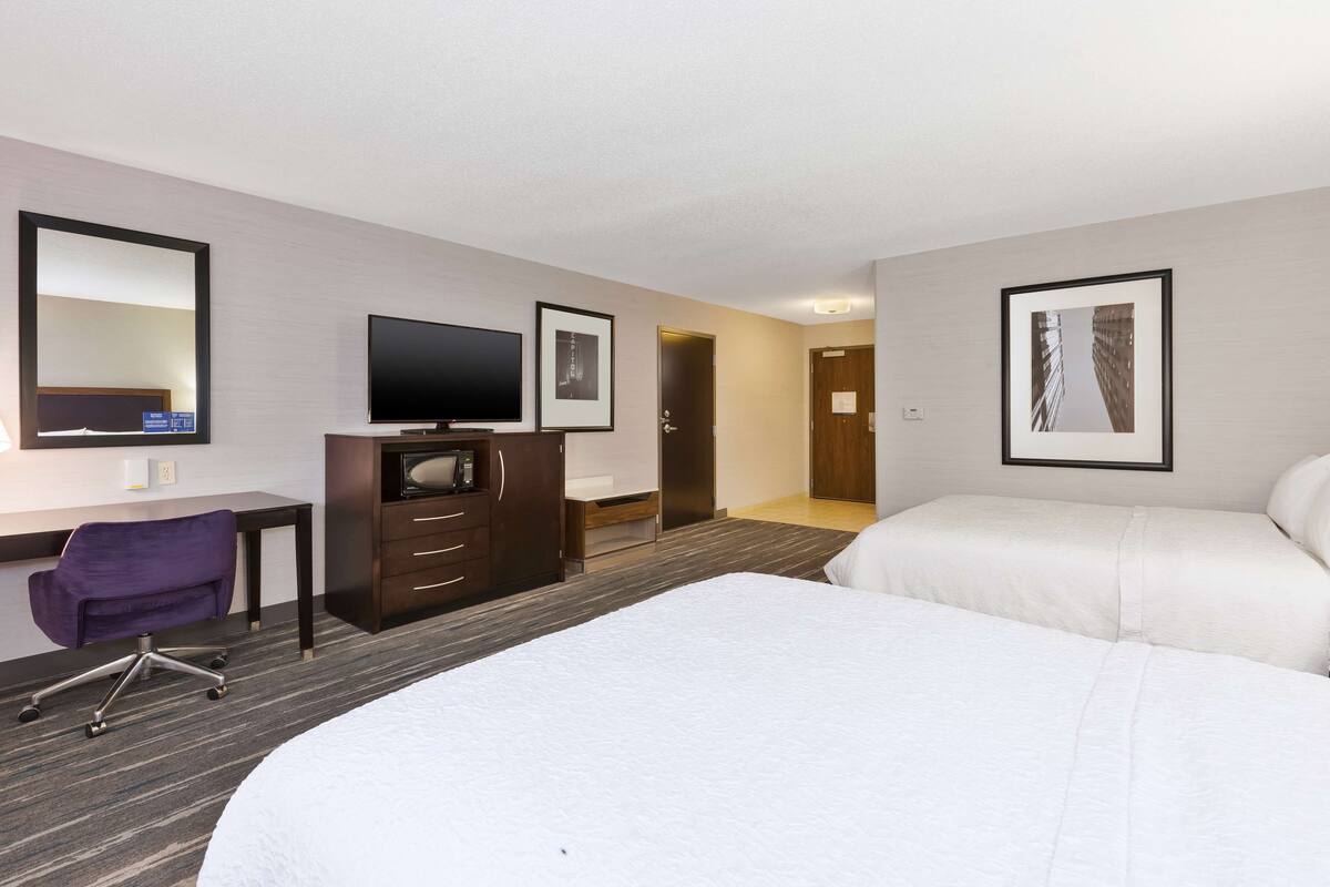 A hotel room with a bed, a desk with a chair, a television, and framed pictures on the wall.