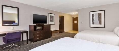 A hotel room with a bed, a desk with a chair, a television, and framed pictures on the wall.
