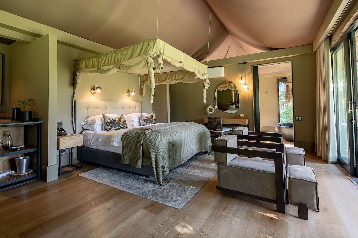 Un dormitorio con cama, mesitas de noche, un escritorio, una silla, un ventanal y vistas al exterior.