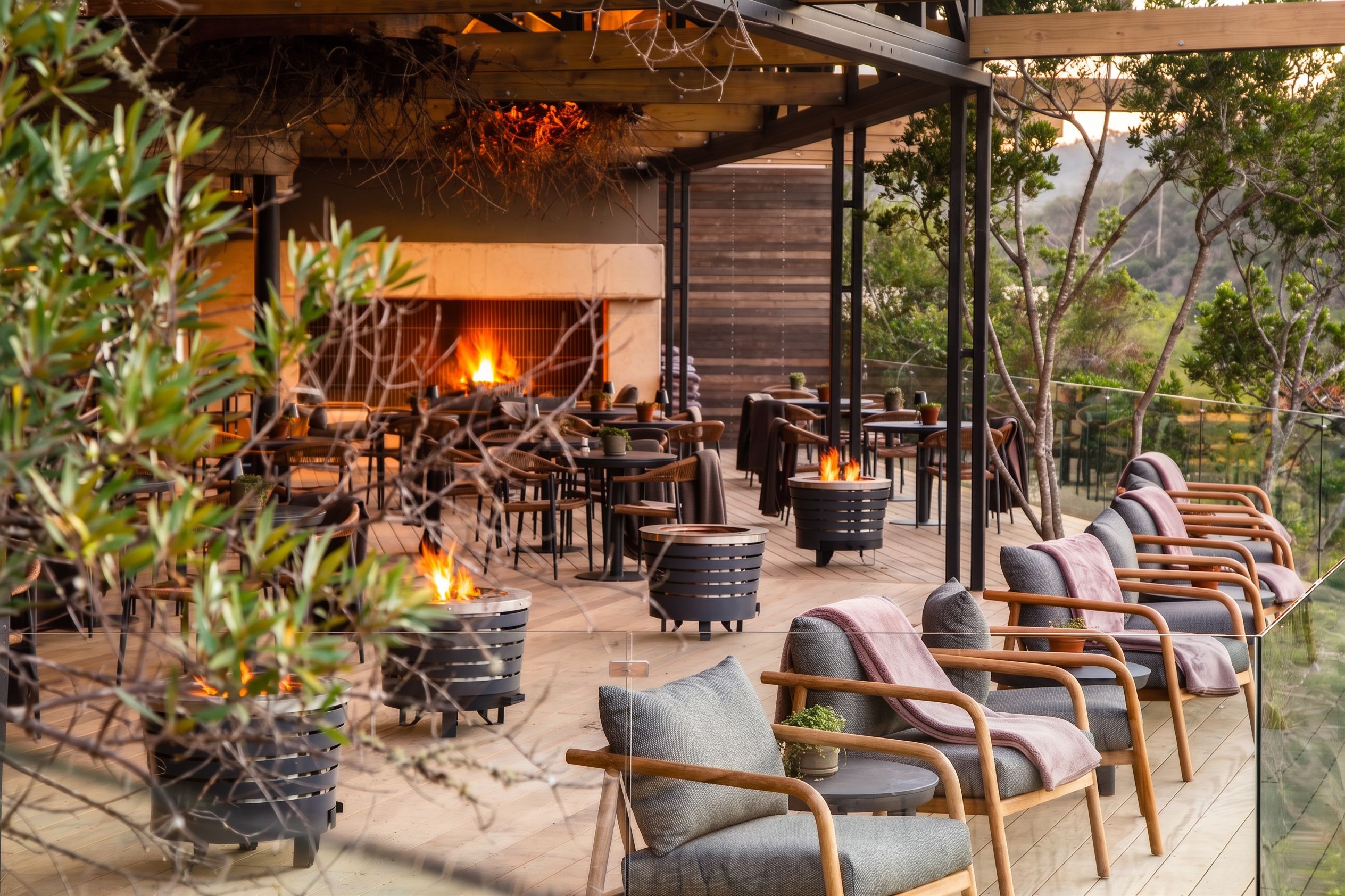 An outdoor seating area with fire pits, wooden chairs, and a view of the surrounding landscape.