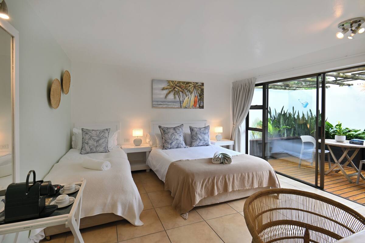A hotel room with two beds, a dining table, and a view of the outdoors.