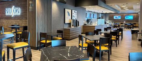 A modern restaurant interior with round tables, yellow cushioned chairs, a counter with a menu display, and a 'Fusion' sign on the wall.