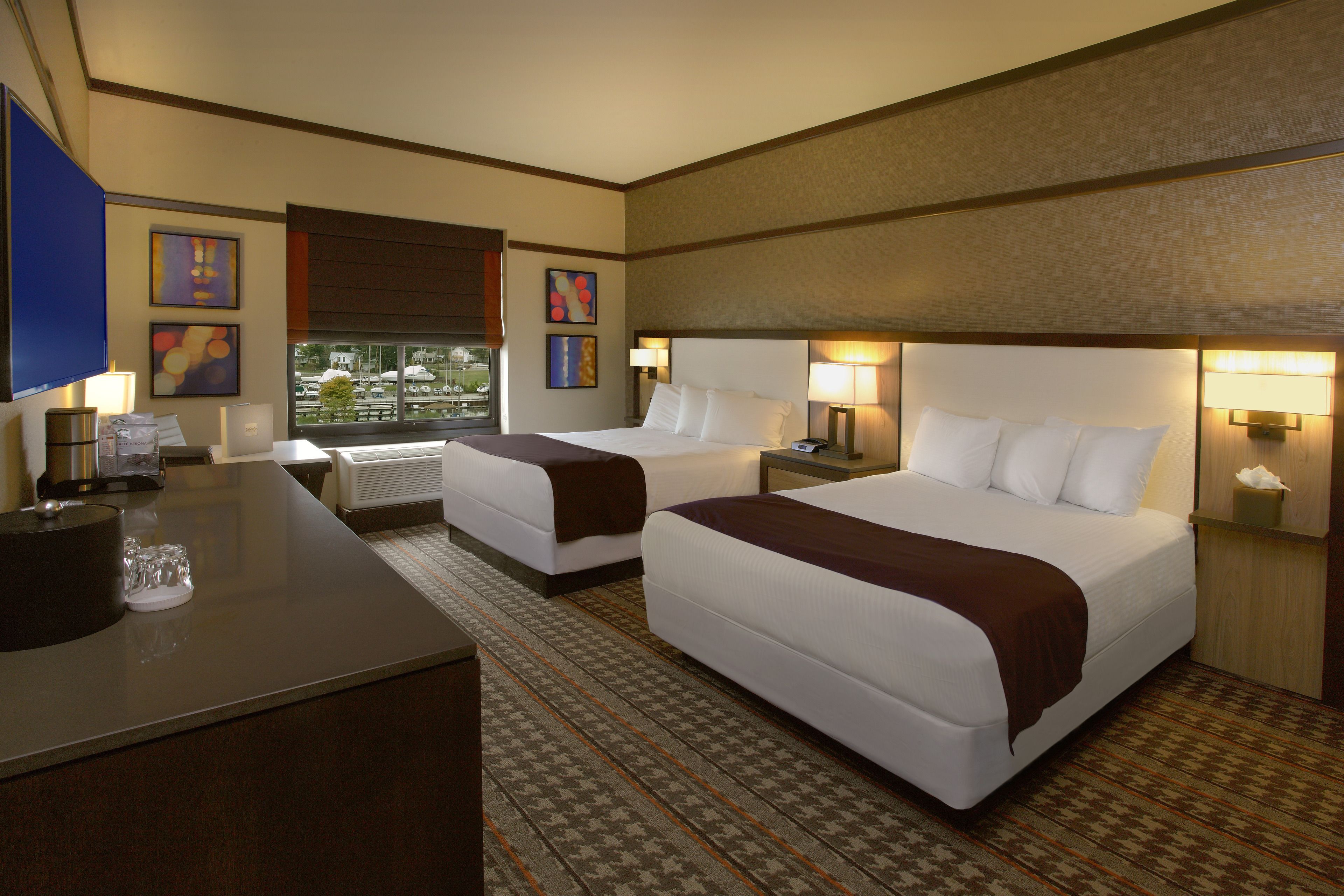 A hotel room with two beds, a desk, and a view of the outdoors.
