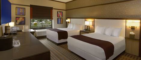 A hotel room with two beds, a desk, and a view of the outdoors.