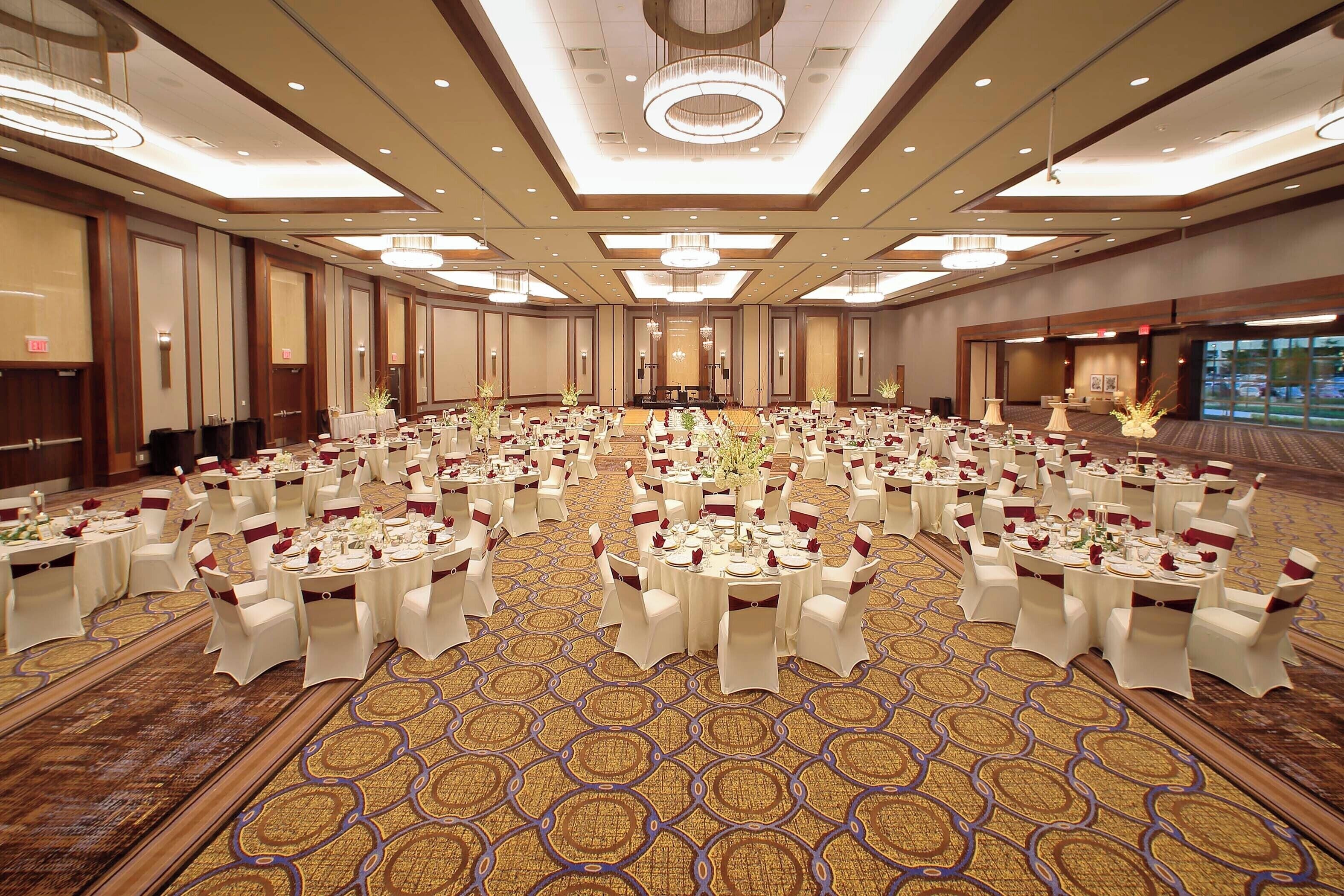 A large banquet hall with round tables set for a formal event, featuring a patterned carpet and modern lighting fixtures.
