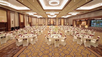 A large banquet hall with round tables set for a formal event, featuring a patterned carpet and modern lighting fixtures.