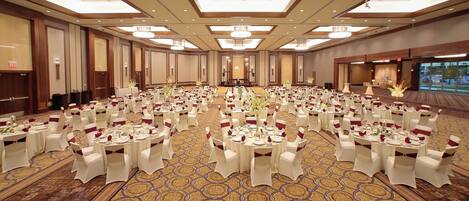 A large banquet hall with round tables set for a formal event, featuring a patterned carpet and modern lighting fixtures.