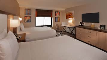A hotel room with two beds, a desk, a chair, a TV, and artwork on the walls.