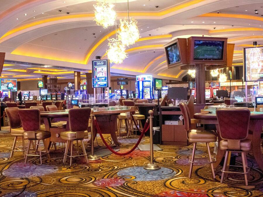 A casino with multiple gaming tables and slot machines, a patterned carpet, and a chandelier.