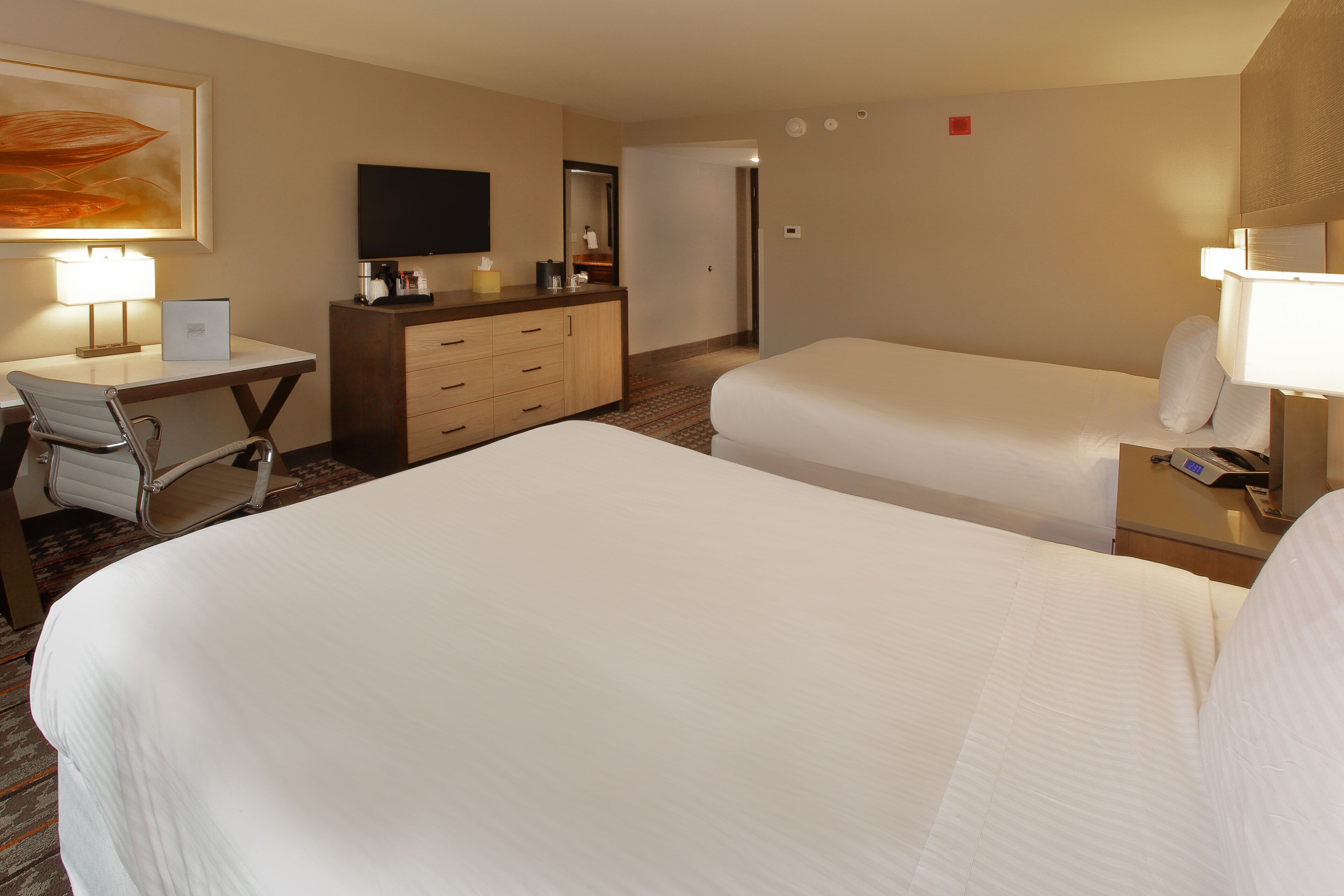 A hotel room with two beds, a desk, a chair, a TV, and a mirror.