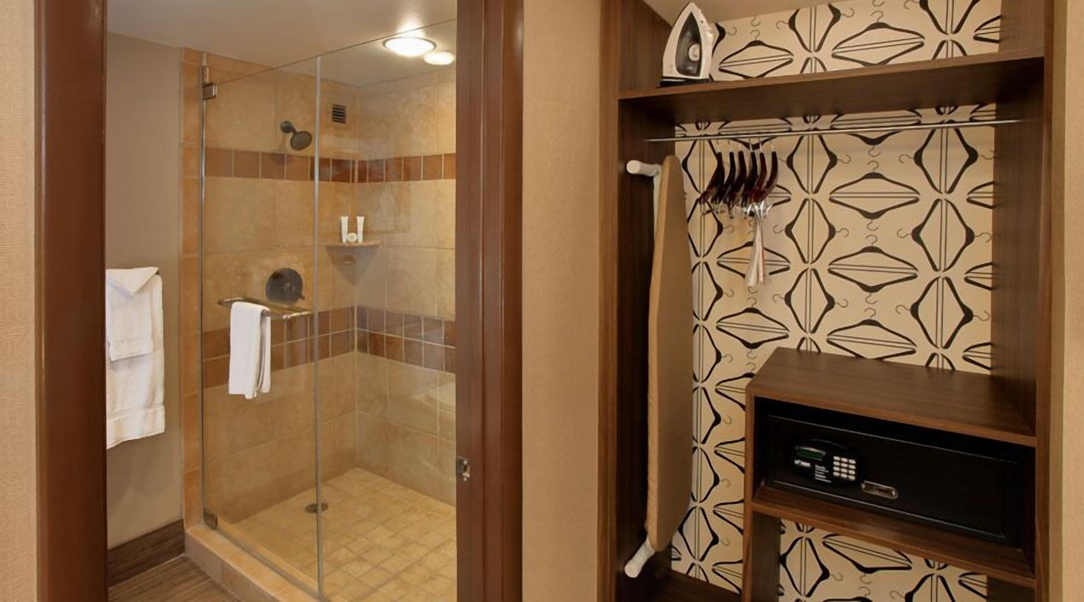 A glass-enclosed shower with a tiled floor, a towel rack, and a small wooden shelf with a microwave.