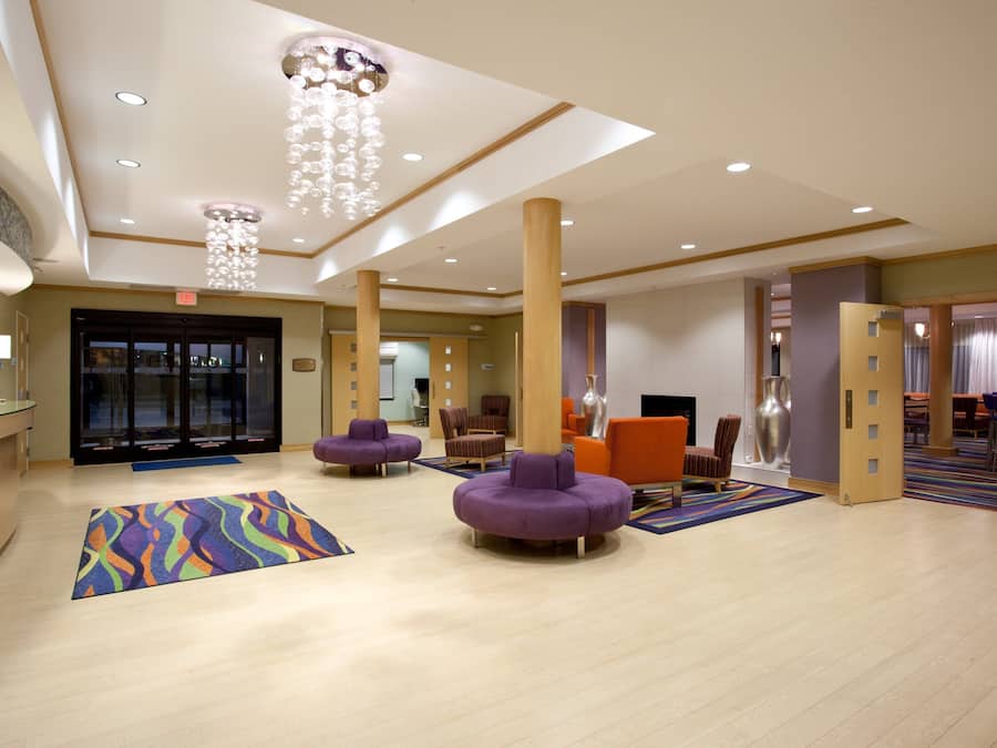 Un hall de hotel con mostrador de recepción, asientos morados, alfombra colorida y un candelabro.
