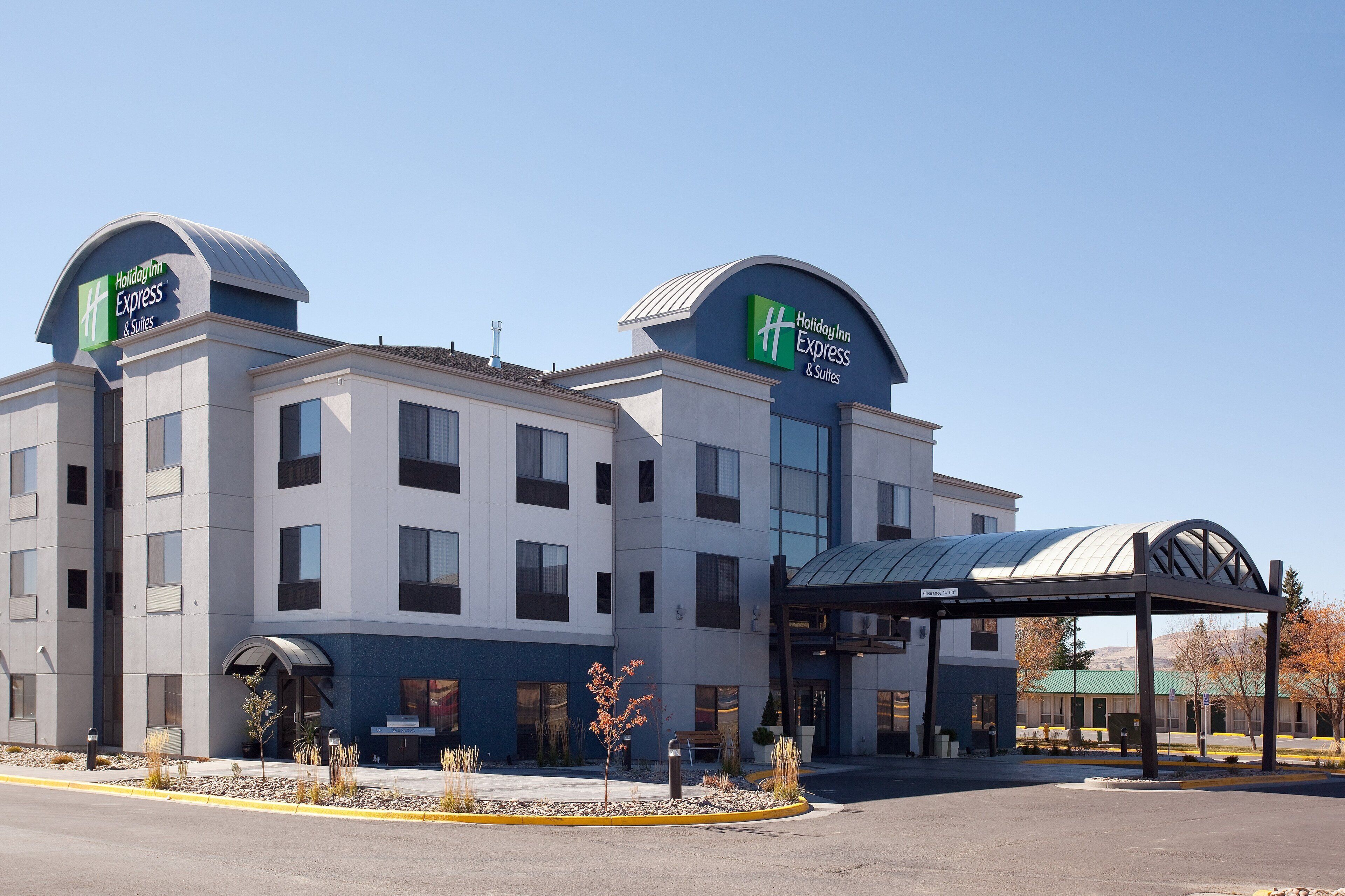 A Holiday Inn Express & Suites hotel with a modern design, featuring a covered entrance and a clear sky.