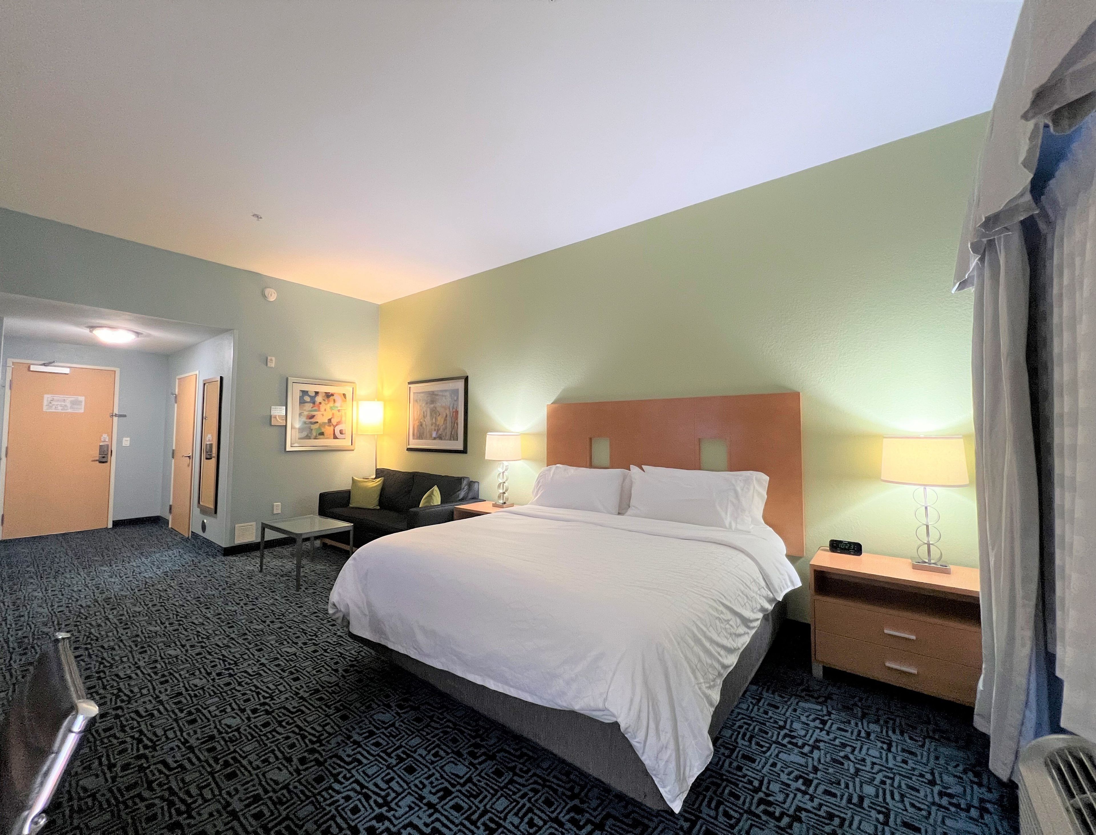 A hotel room with a bed, bedside tables, a desk, a chair, and a couch.