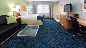 A hotel room with a bed, a desk with a computer, a sofa, and a coffee table.