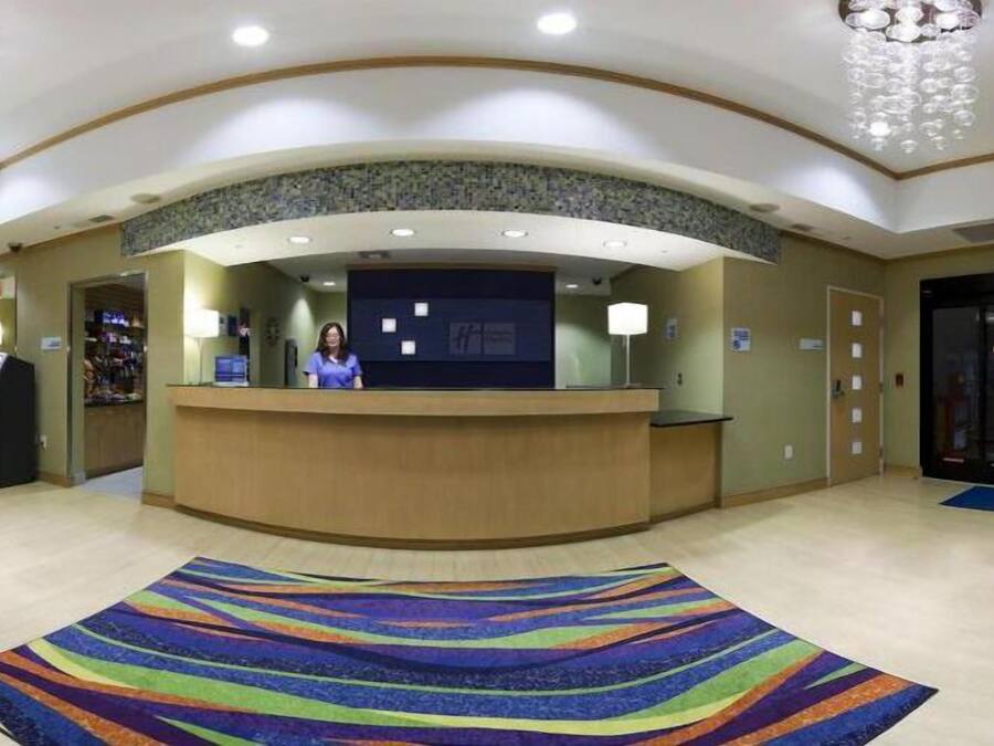 A hotel reception area with a curved reception desk, a receptionist, a self-service kiosk, and a colorful striped carpet.