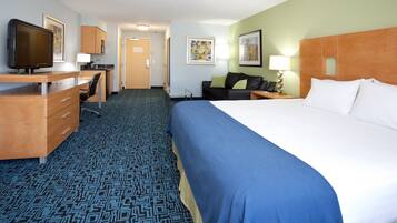 A hotel room with a large bed, a desk with a computer, a television, and a small kitchenette.