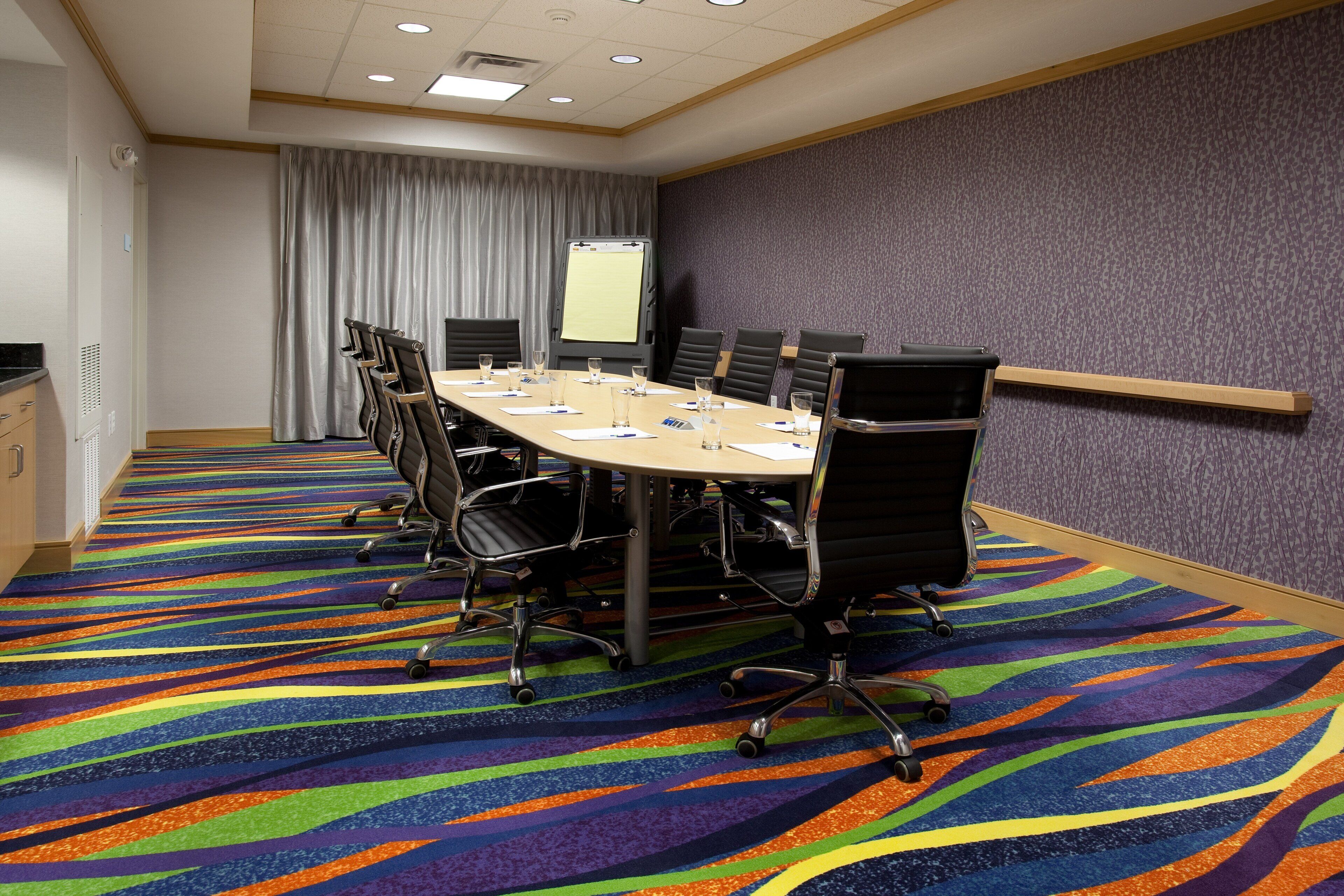 A conference room with a large table, chairs, a projector screen, and a patterned carpet.