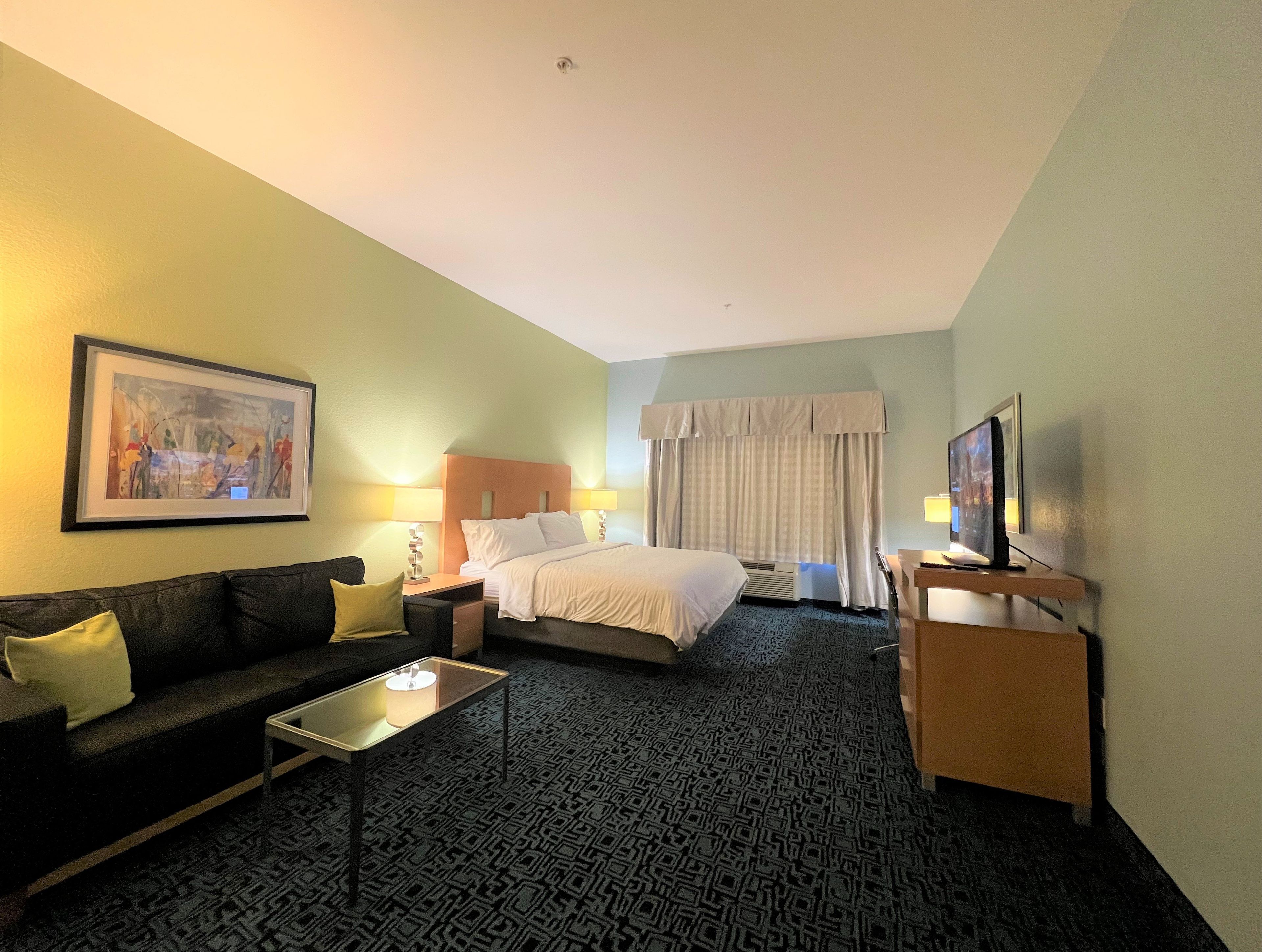 A hotel room with a bed, a sofa, a TV, and a painting on the wall.