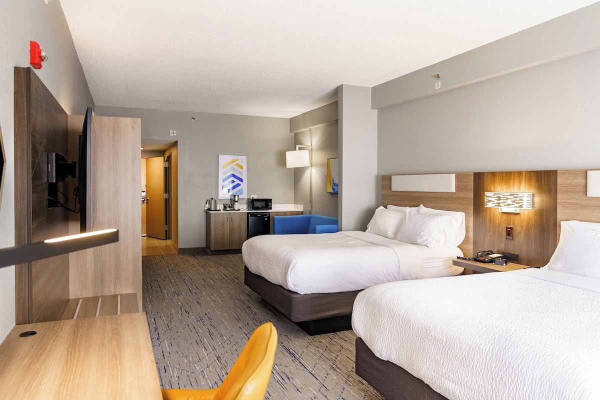 A hotel room with two beds, a desk, a TV, a microwave, and a bathroom visible in the background.