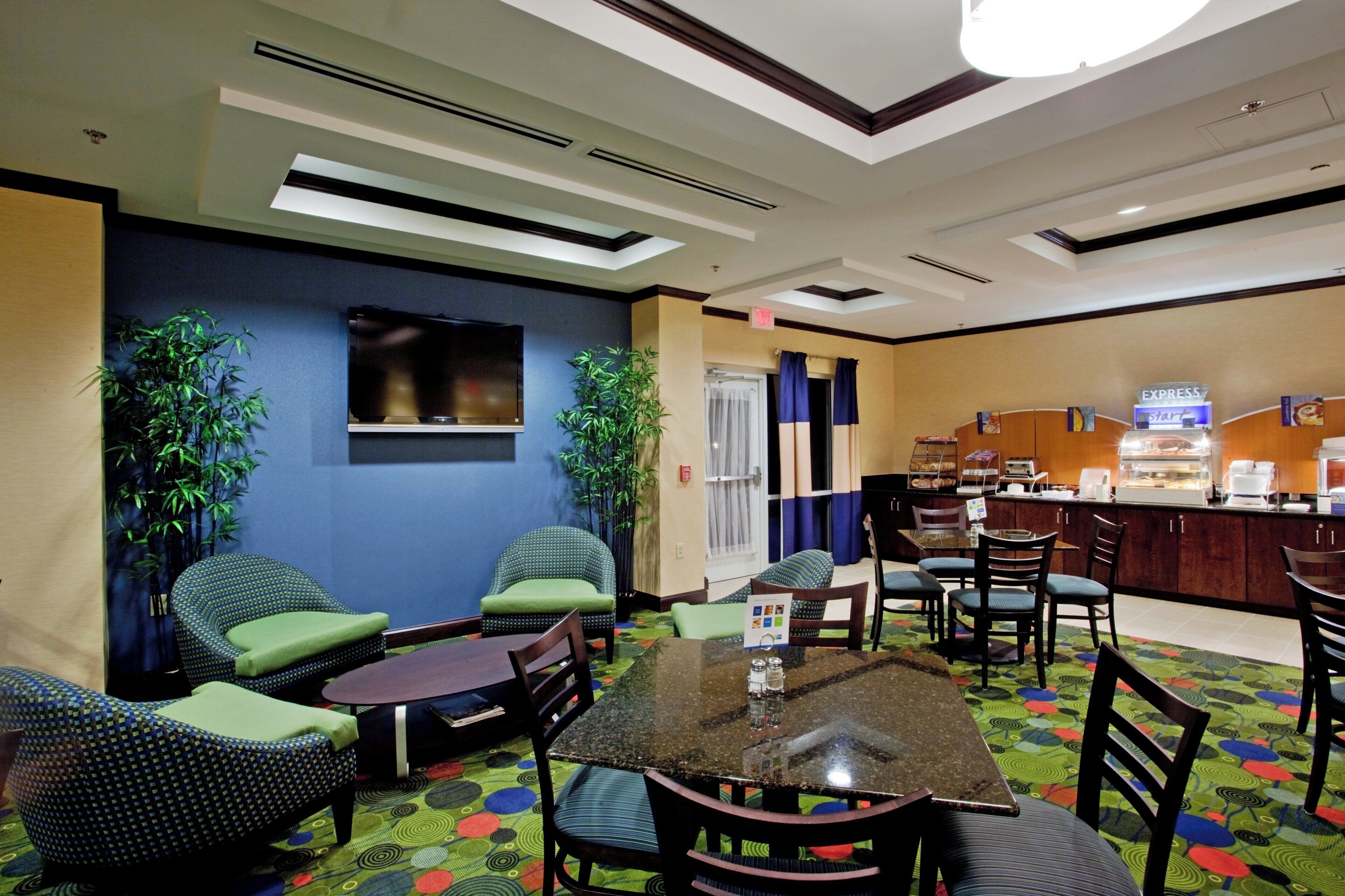 Un vestíbulo de hotel con asientos, televisión, zona de buffet y mostrador de recepción.