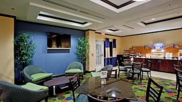 Un vestíbulo de hotel con asientos, televisión, zona de buffet y mostrador de recepción.