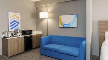 A hotel room with a kitchenette, a blue sofa, and two abstract paintings on the wall.