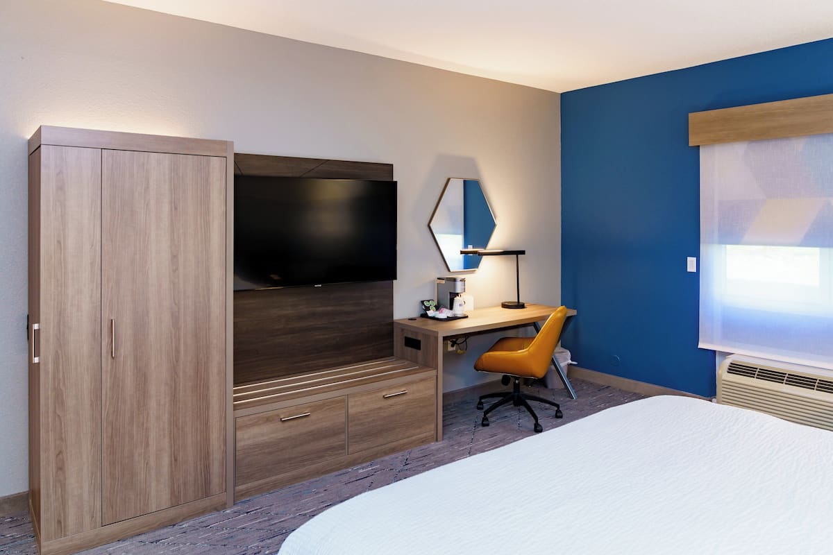 A bedroom with a bed, a desk with a chair, a TV, and a wardrobe.