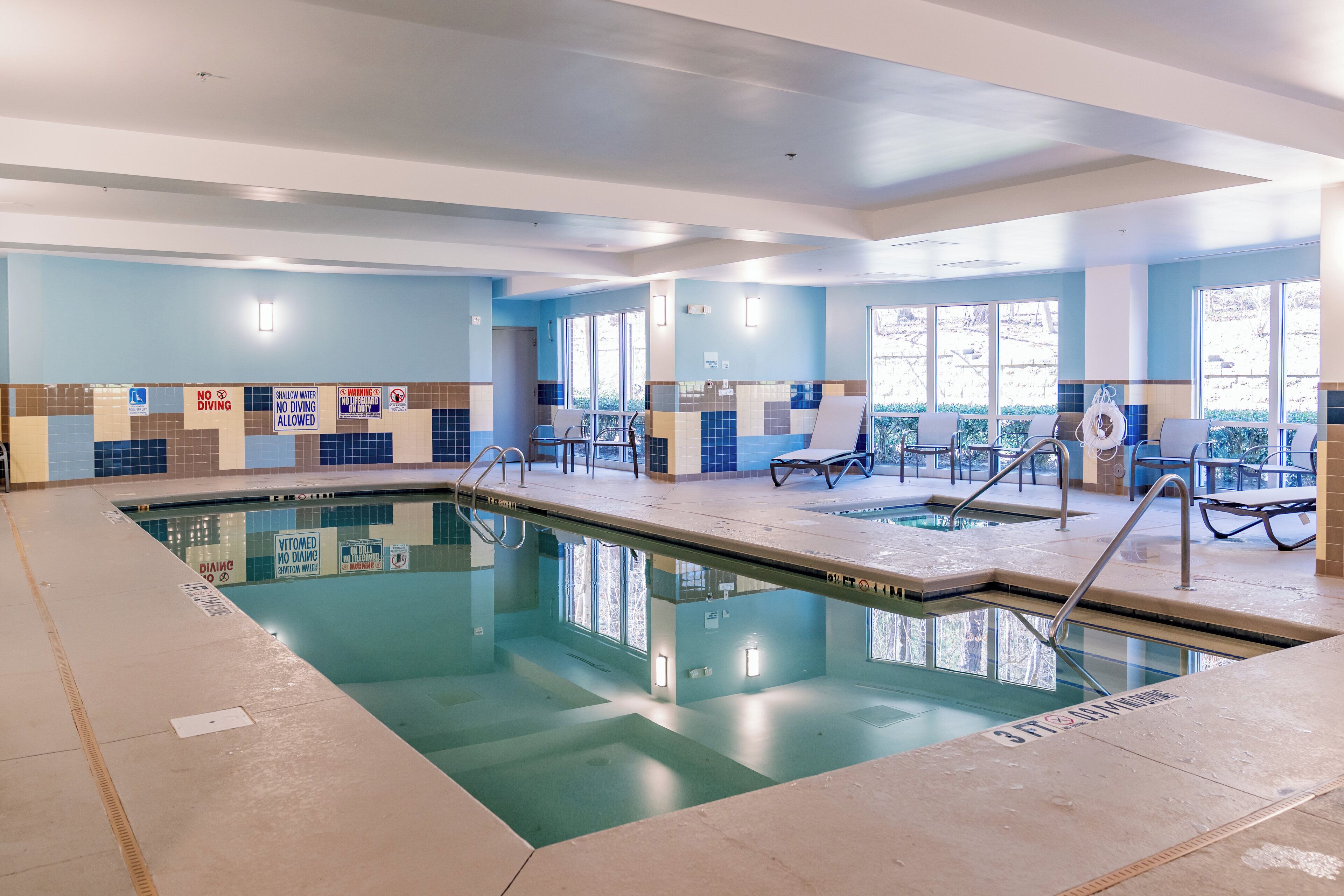 An indoor swimming pool with clear water, tiled walls, and a few lounge chairs.