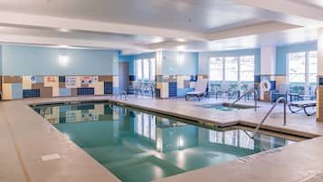 An indoor swimming pool with clear water, tiled walls, and a few lounge chairs.