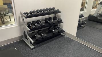 Un gimnasio con un banco de pesas mancuernas y una cinta de correr al fondo.