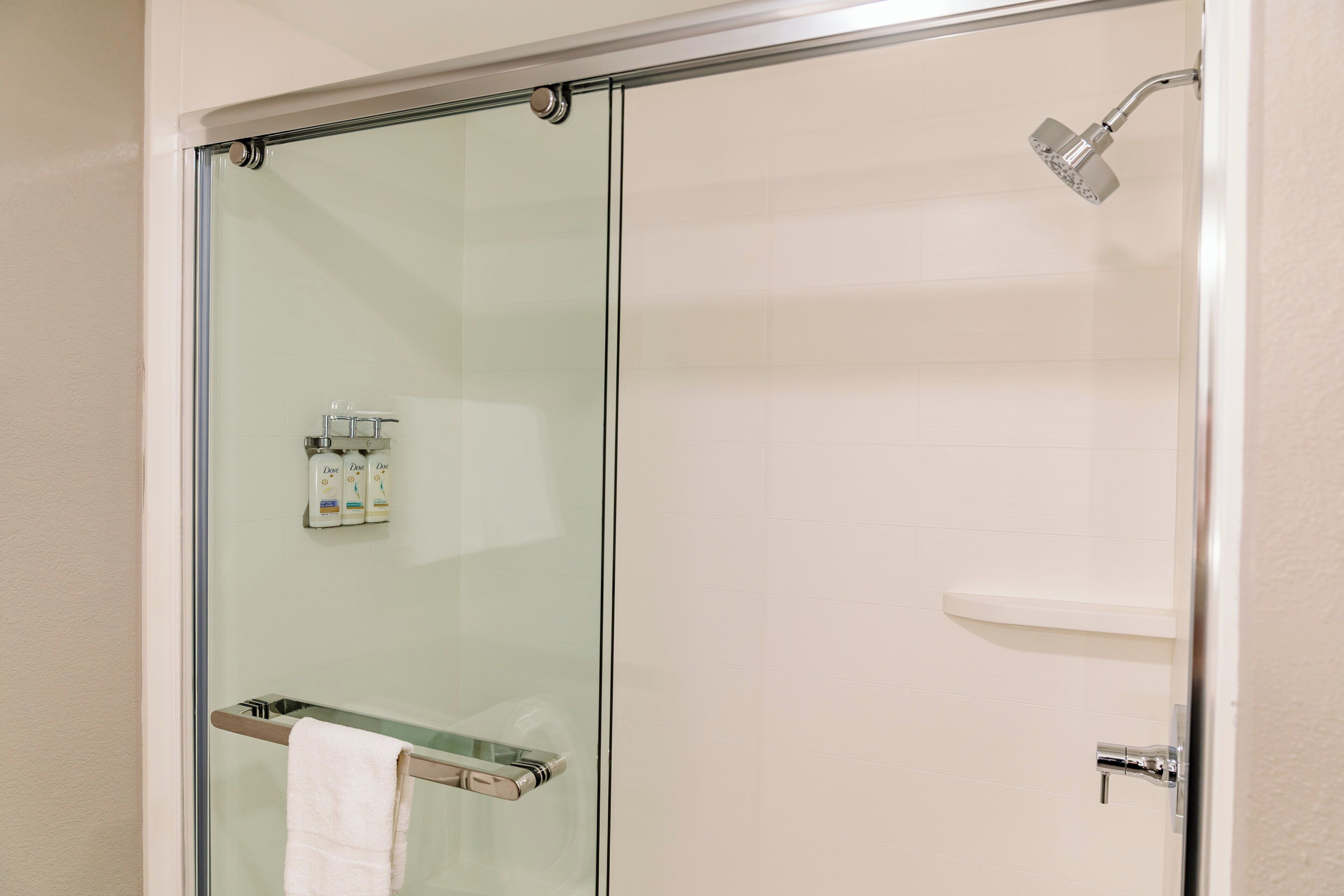 A glass-enclosed shower with a handheld showerhead, a towel rack with a white towel, and a small shelf with toiletries.
