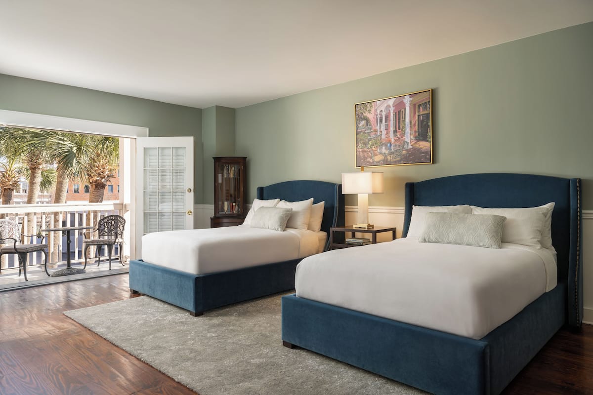 A bedroom with two beds, a balcony with chairs, and a painting on the wall.