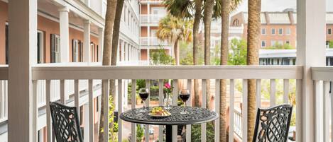 Een balkon met een ronde tafel, twee stoelen, een schaal fruit en twee wijnglazen.