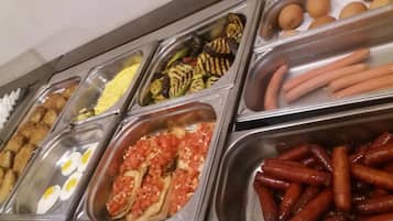 Un bufé con diversas opciones de comida, incluyendo huevos, salchichas y verduras.