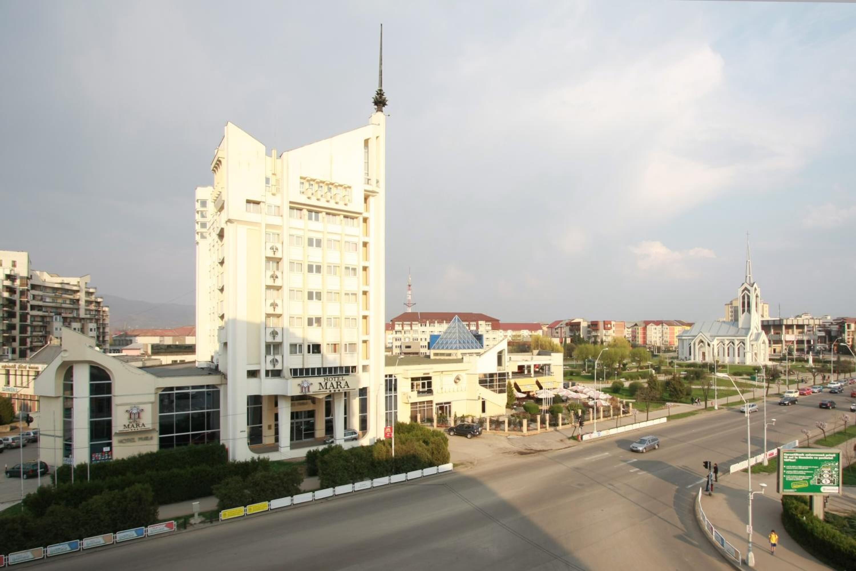 Un hotel moderno con una torre destacada y una iglesia al fondo.