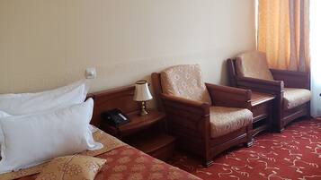 A hotel room with two beds, a nightstand with a lamp, a chair, and an air conditioning unit.