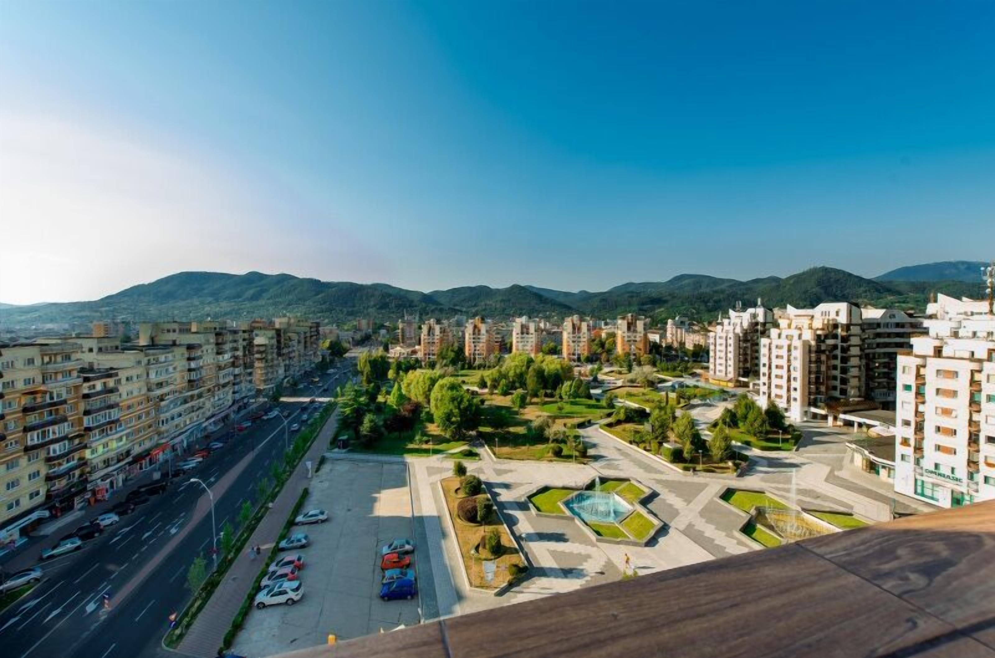 Un barrio residencial con edificios de apartamentos de varios pisos, un parque central con senderos y una calle con automóviles estacionados.
