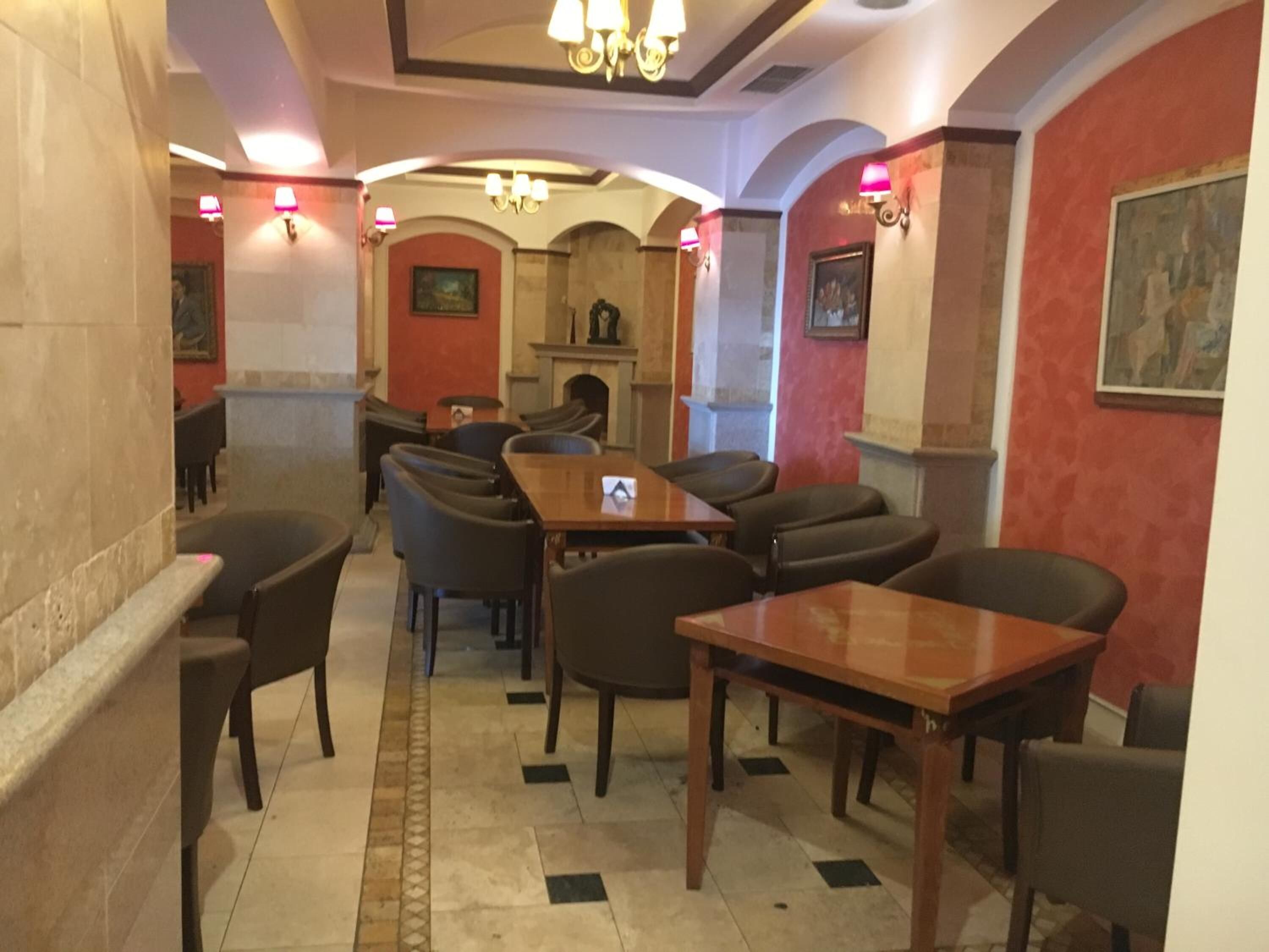 En restaurant med en central pejs, flere borde og stole, samt vægmonteret belysning.